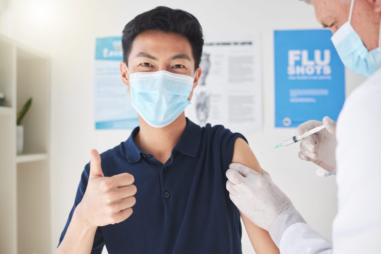 young man giving a thumbs up sign while getting vaccinated