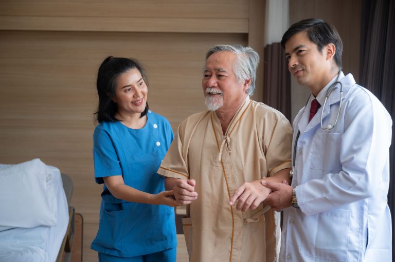 two healthcare professionals assisting an elderly male patient