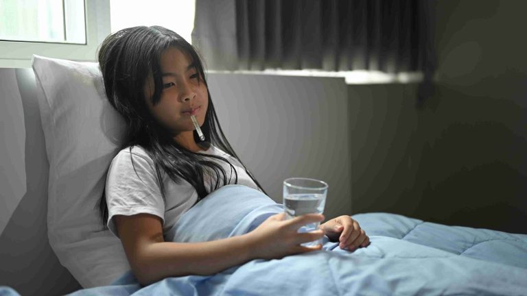 little girl with fever lying in bed holding a glass of water