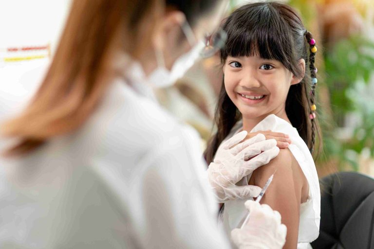 little girl smiling at the camera while getting vaccinated