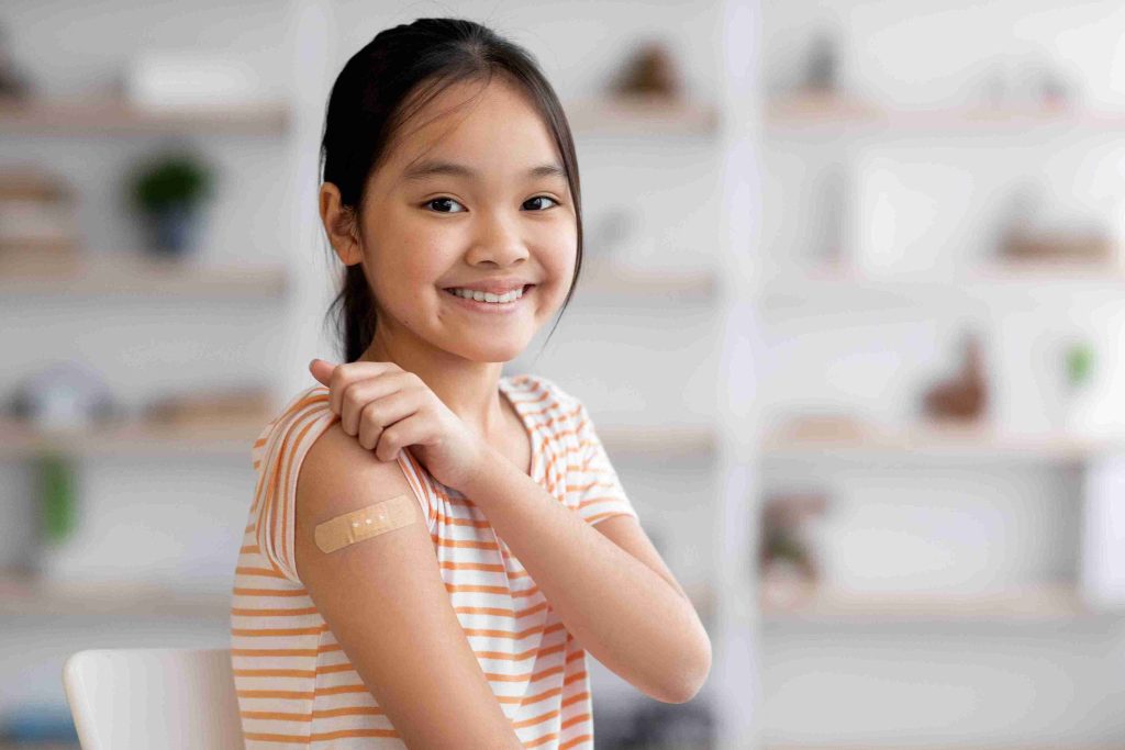 Young Asian girl smiling and showing off her vaccination.