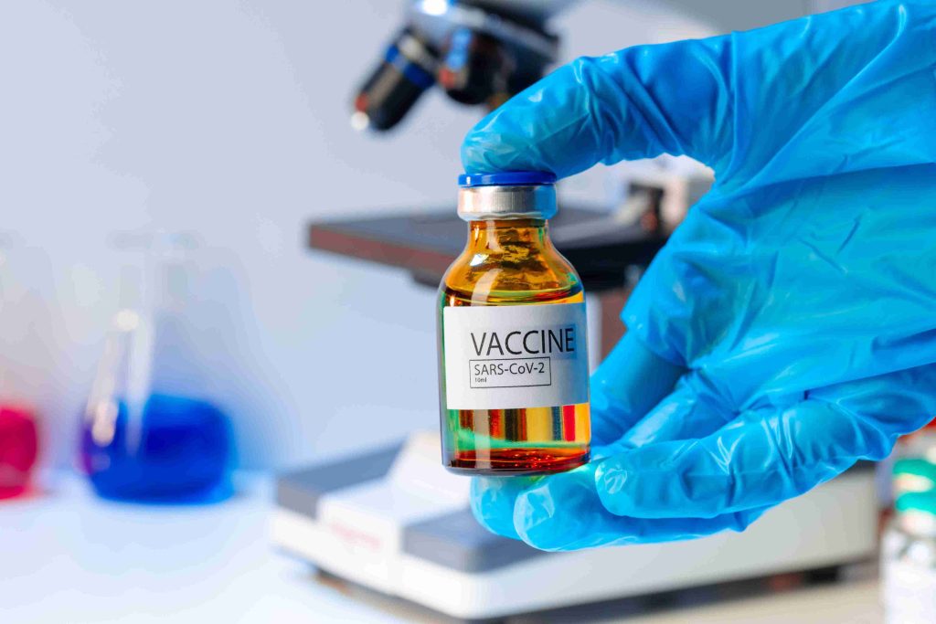Hand wearing a blue glove holding a covid vaccine vial.