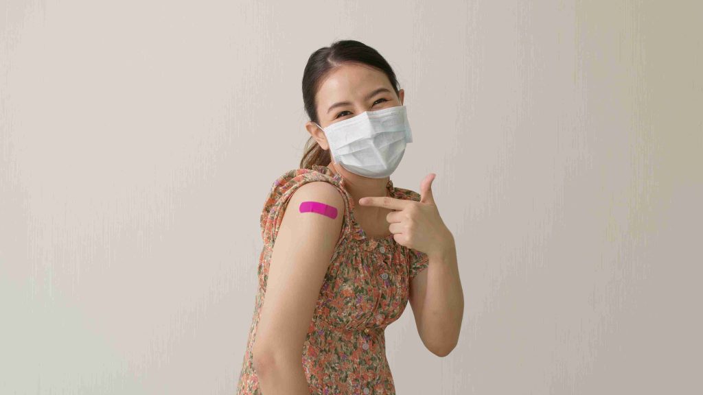 Young woman wearing a face mask and showing off her flu vaccination.