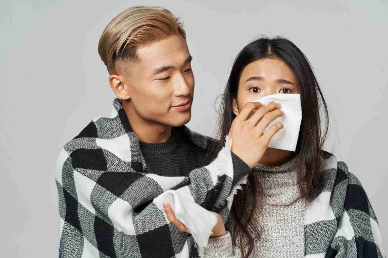 Man covering his girlfriend's nose and mouth with tissue.