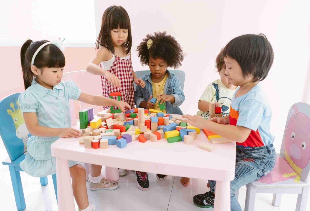 Kids sitting and playing around a table with colorful blocks.