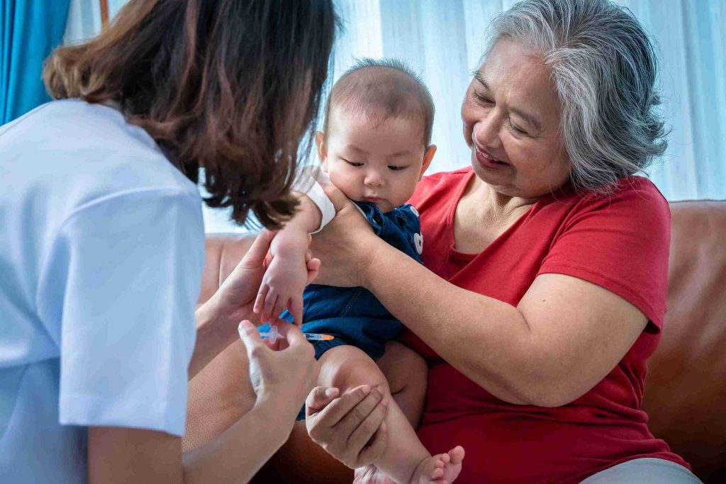 Infant held by grandmother for immunization.