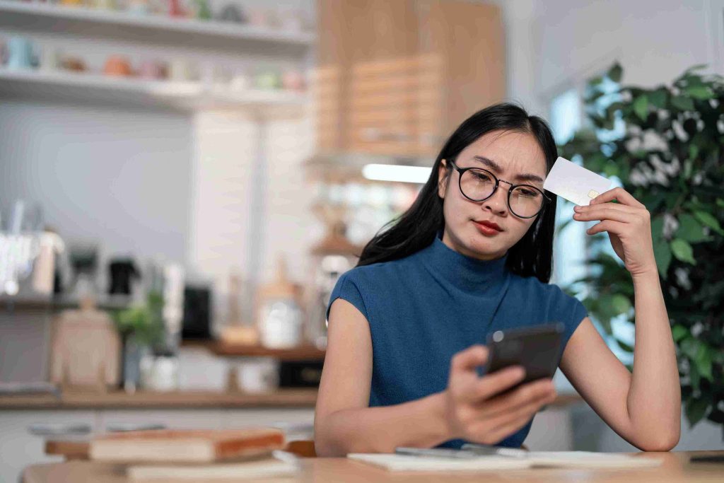 Woman holding a card, looking at her phone and thinking.