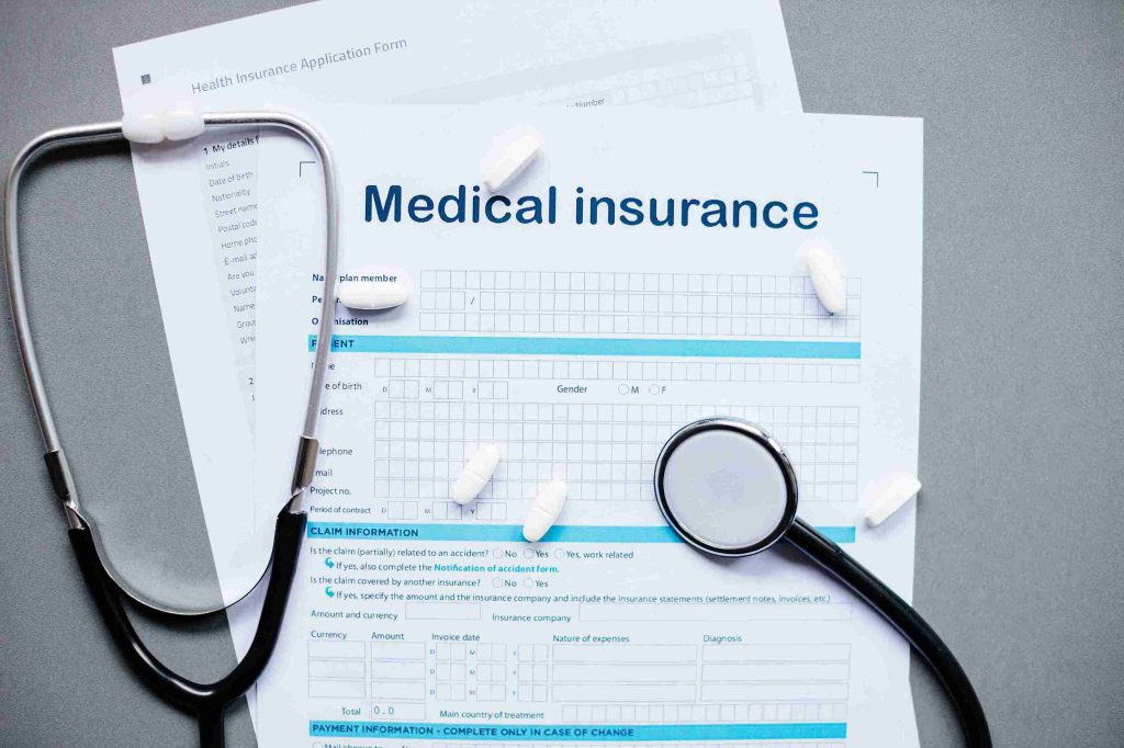 Image of a medical insurance form with tablets and stethoscopy on top.