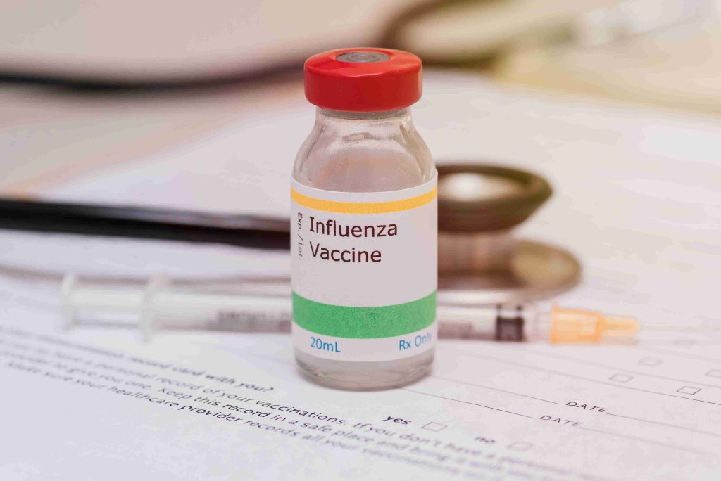 Image of an influenza vaccine with a syringe and stethoscope behind it.