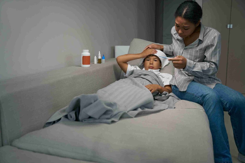 Woman checking the temperature of a boy lying on the couch.