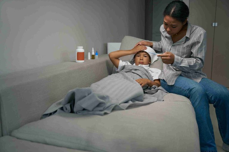 Woman checking the temperature of a boy lying on the couch.