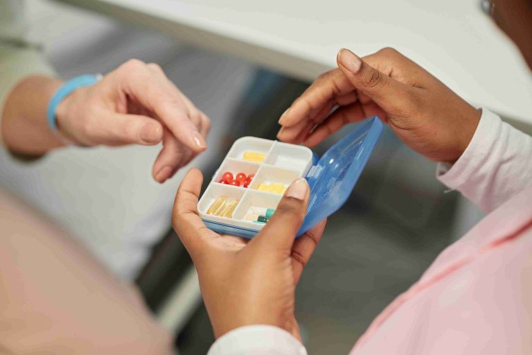 Image of a hand holding a pill dispenser with vitamins inside.